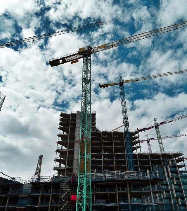 Urban construction site with numerous cranes framing rising skyscrapers against a blue sky.